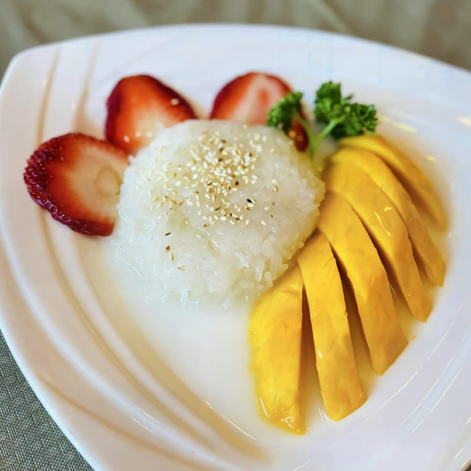 Thai mango sticky rice dessert with sliced strawberries and parsley on a white plate.