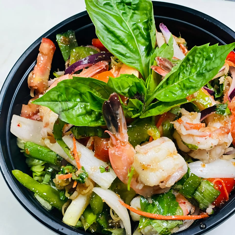 Close-up of a vibrant Thai salad with shrimp, green vegetables, red onions, and fresh basil.