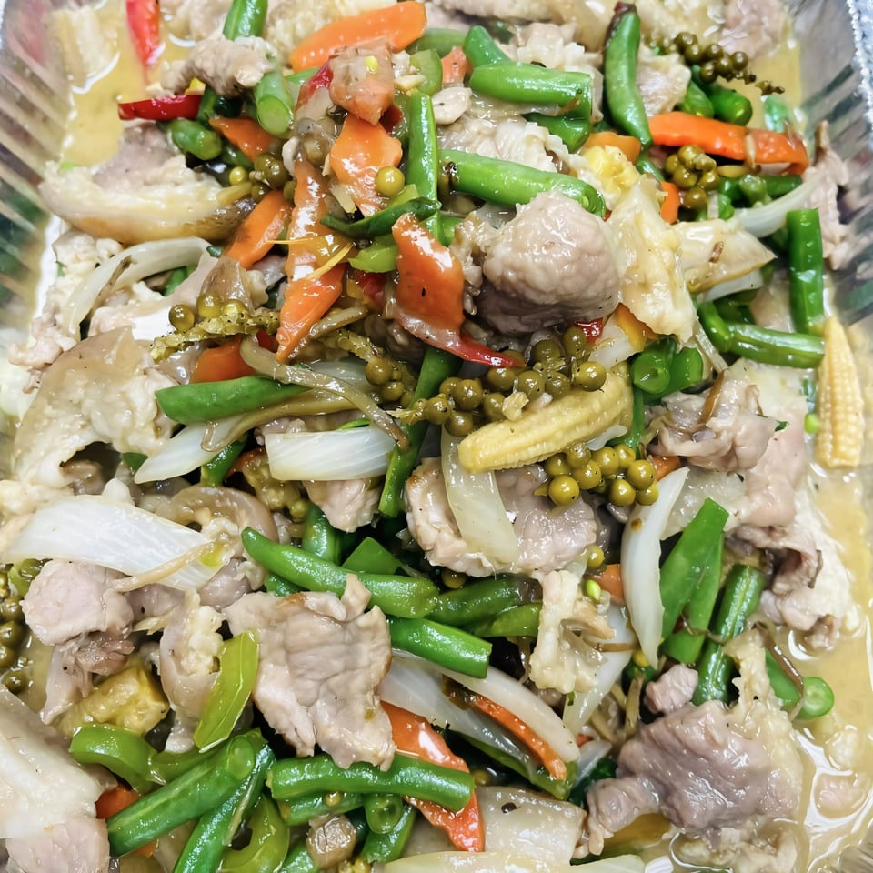 Close-up of Thai stir-fried pork with green beans, carrots, onions, and green peppercorns.