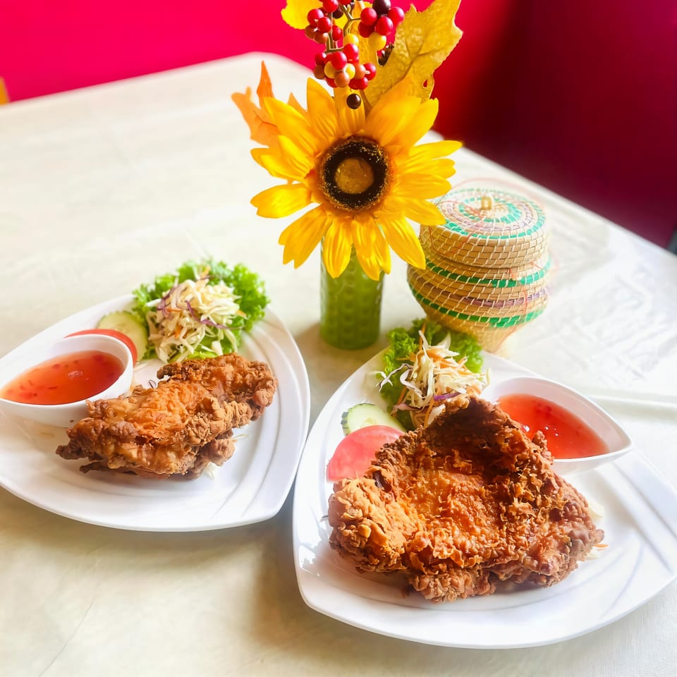Two plates of crispy fried chicken with salad and sweet chili sauce, next to a sunflower decoration.