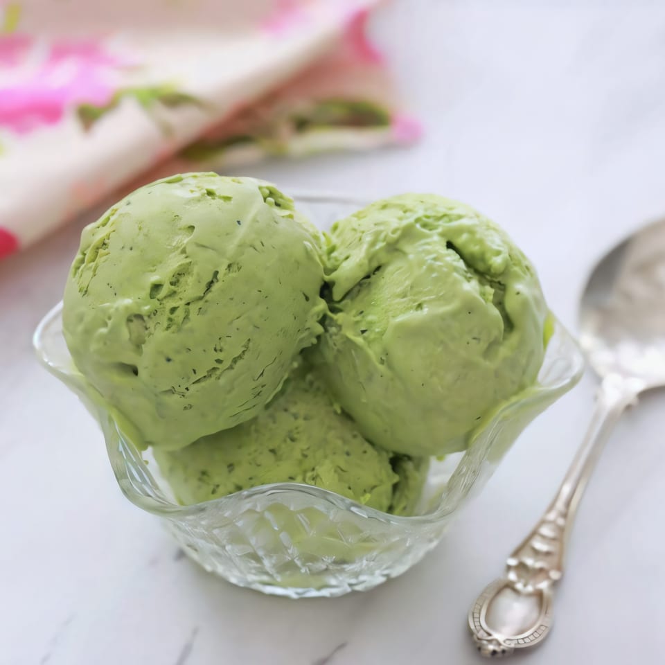 Three scoops of vibrant green matcha ice cream in a clear glass bowl with a spoon.